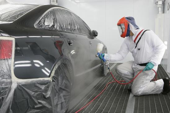 A painter in a spray booth spraying a car